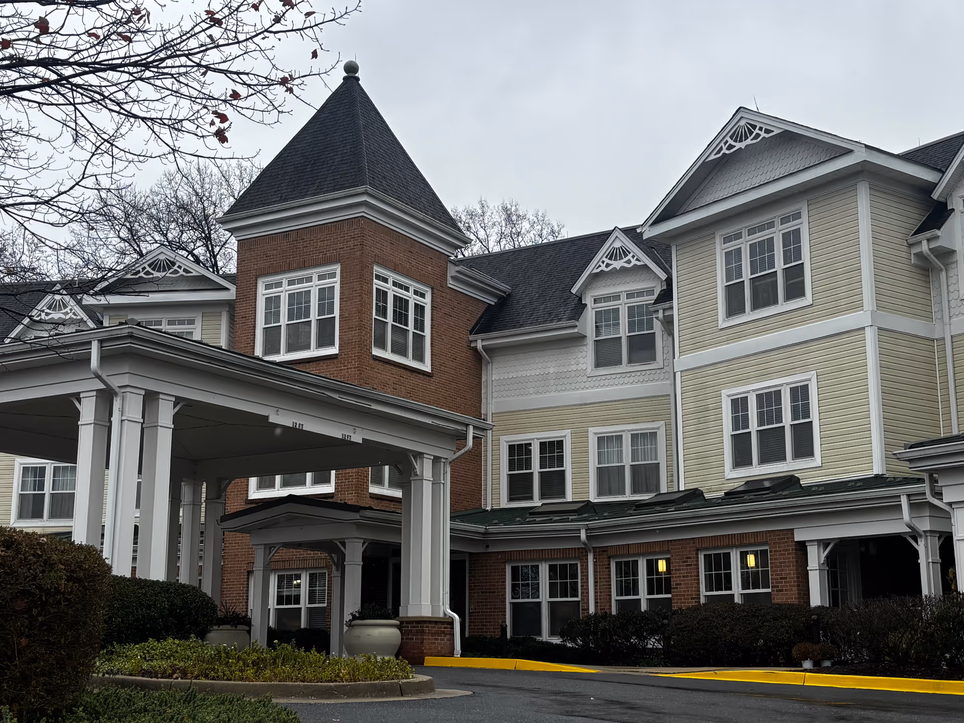 Front entrance of a multi-story senior living building with a covered porte-cochère and decorative turret.