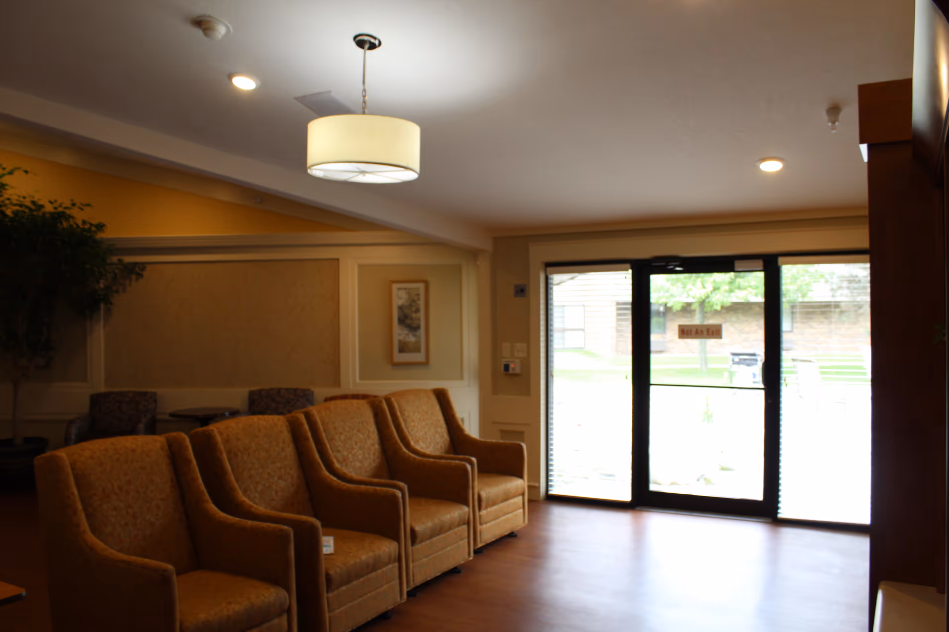 Lobby seating area with a row of upholstered armchairs, overhead lighting, and glass entry doors.
