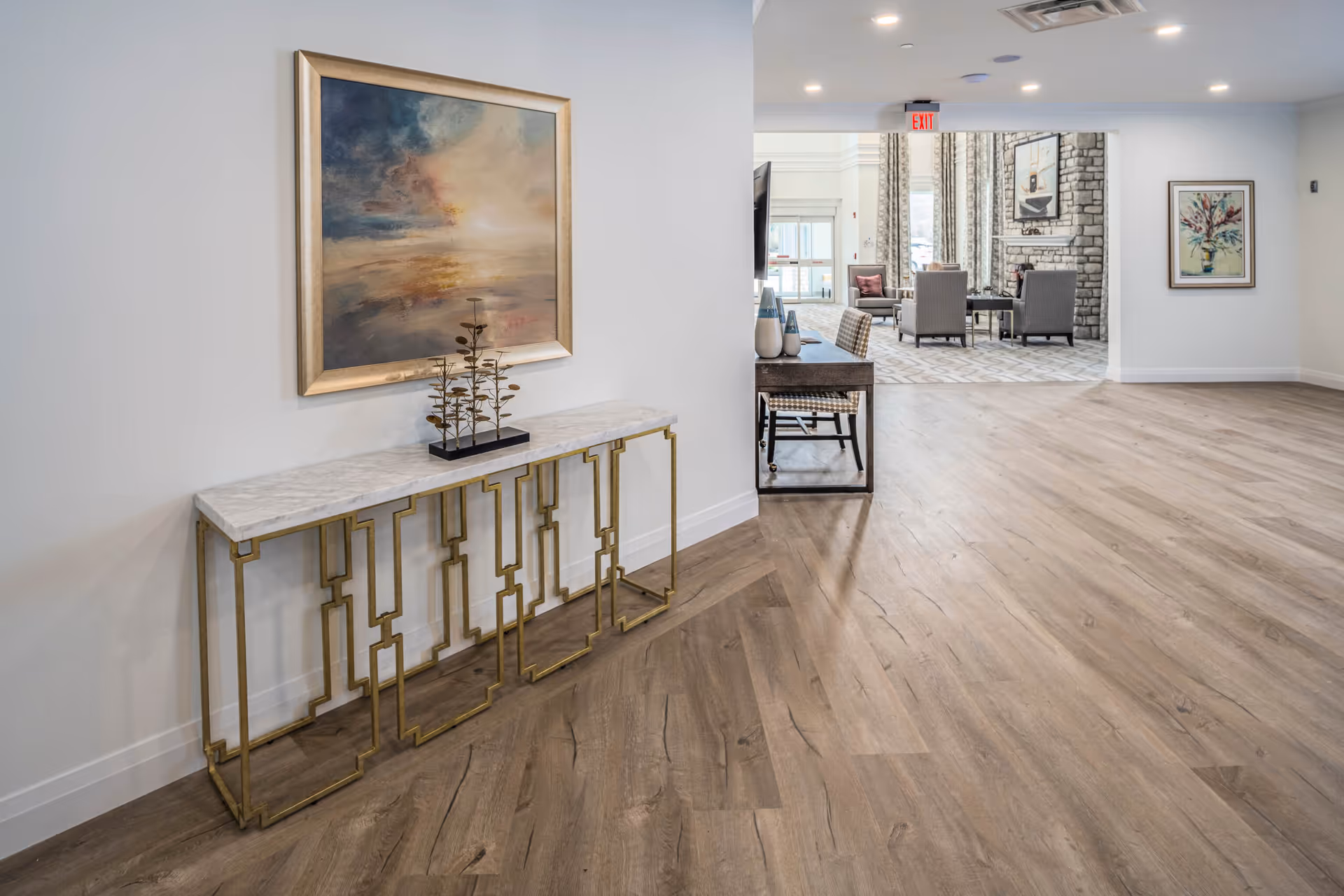 Bright lobby hallway with a marble-topped console table and framed artwork leading into a furnished seating area with chairs and a fireplace.