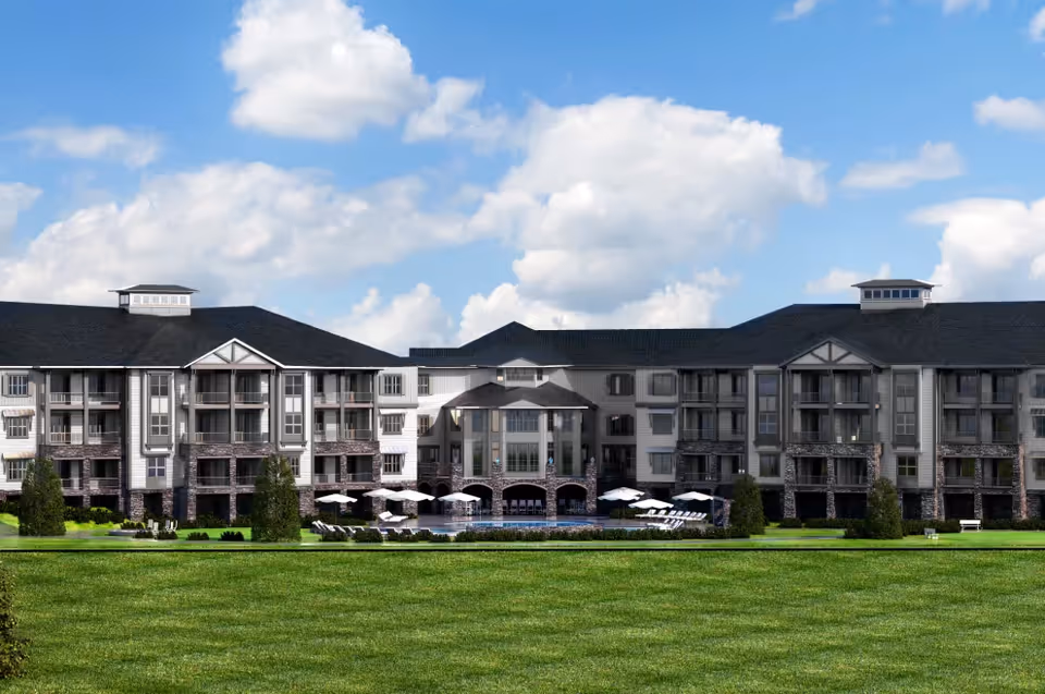 Front exterior of a large multi-story senior living building with balconies, a lawn and pool under a partly cloudy sky.