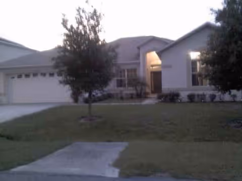 Front exterior of a single-story senior living facility with a driveway, lawn, and trees.