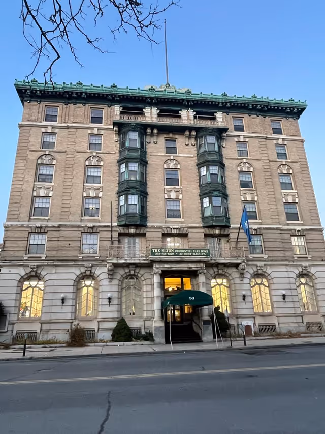 Front facade of a multi-story historic brick residential care building with a green awning and a sign reading "The Elton Residential Care Home."