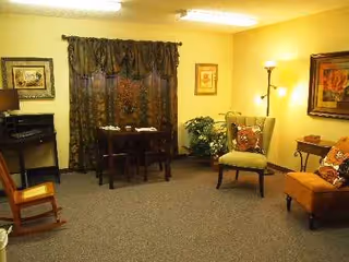 Cozy senior living room with seating, a table, piano, curtains, and wall art.