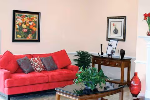 Bright living room area with a red sofa, plants, framed art, and a wooden console table.