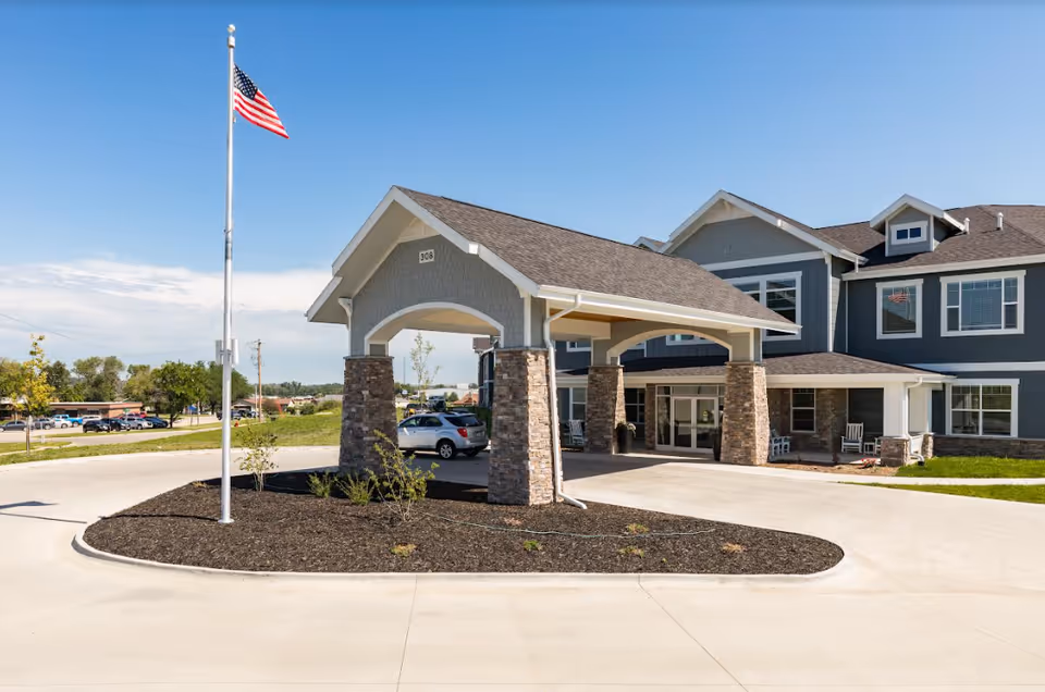 Front exterior of Birkwood Village Tama-Toledo, a blue-gray senior living building with stone pillars and entrance.