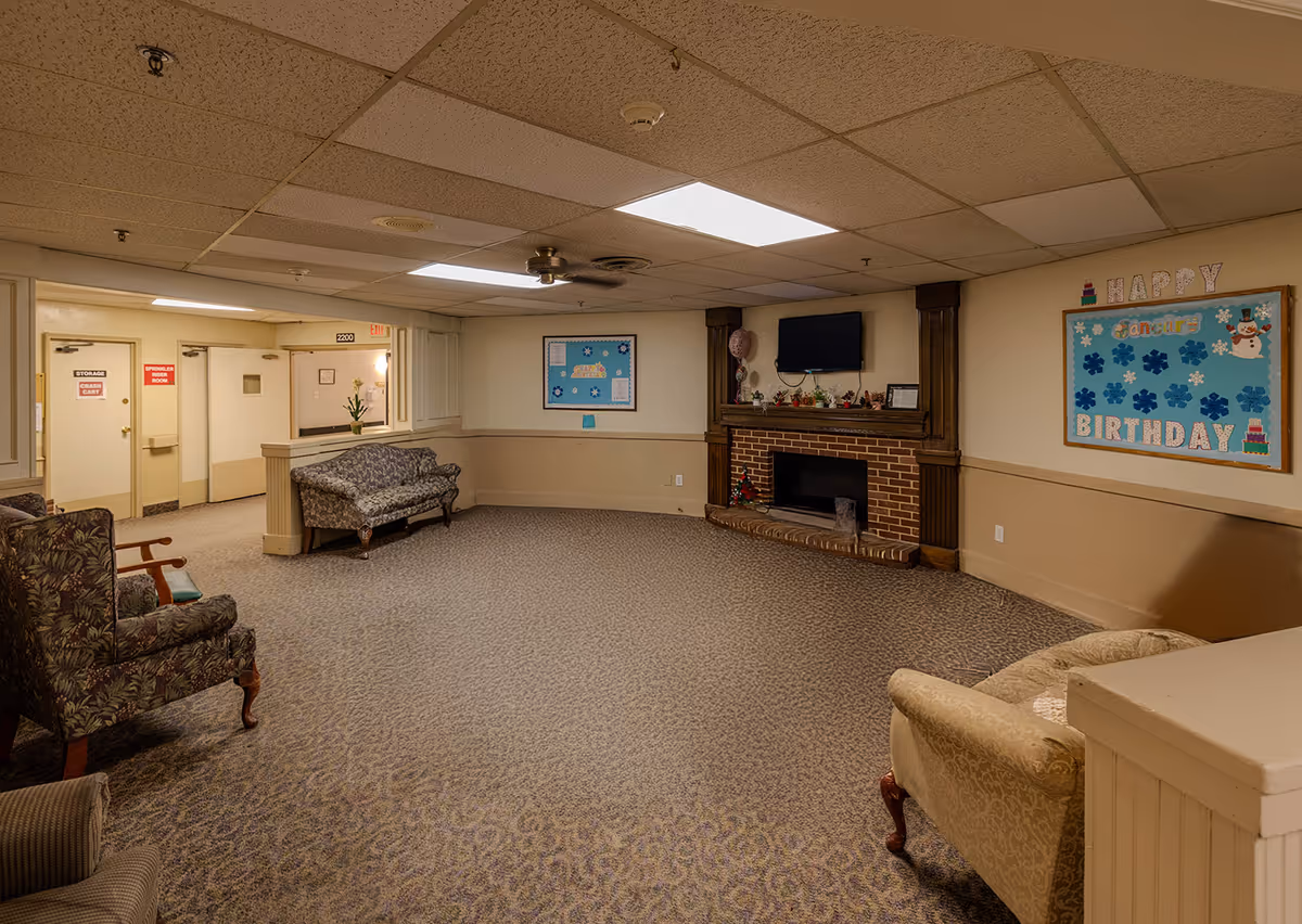 Spacious senior living facility lounge with seating, a brick fireplace, and a birthday-themed wall display.