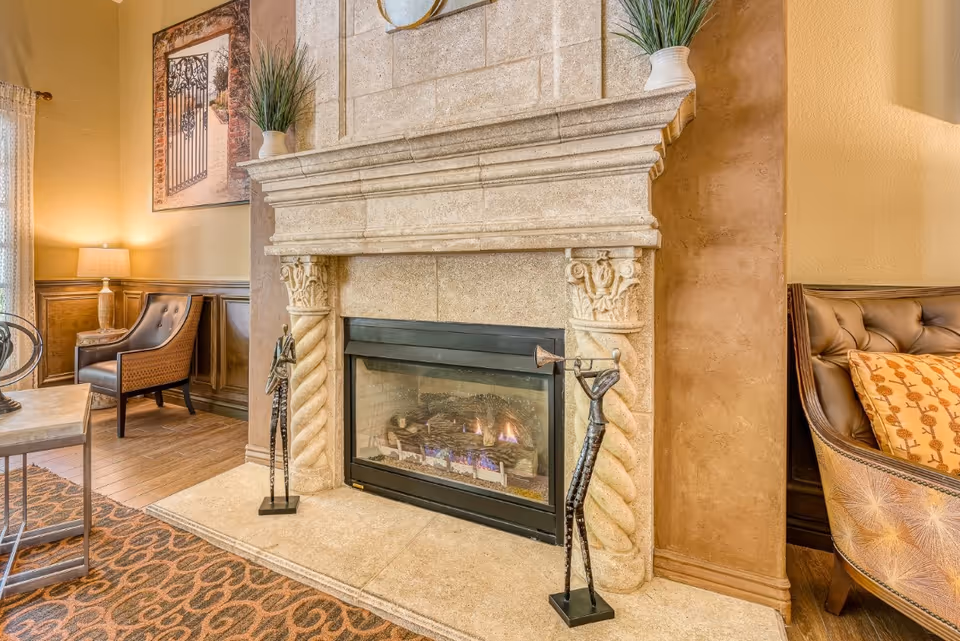 Interior living area featuring an ornate stone fireplace with a lit gas fire, decorative sculptures, and upholstered chairs.