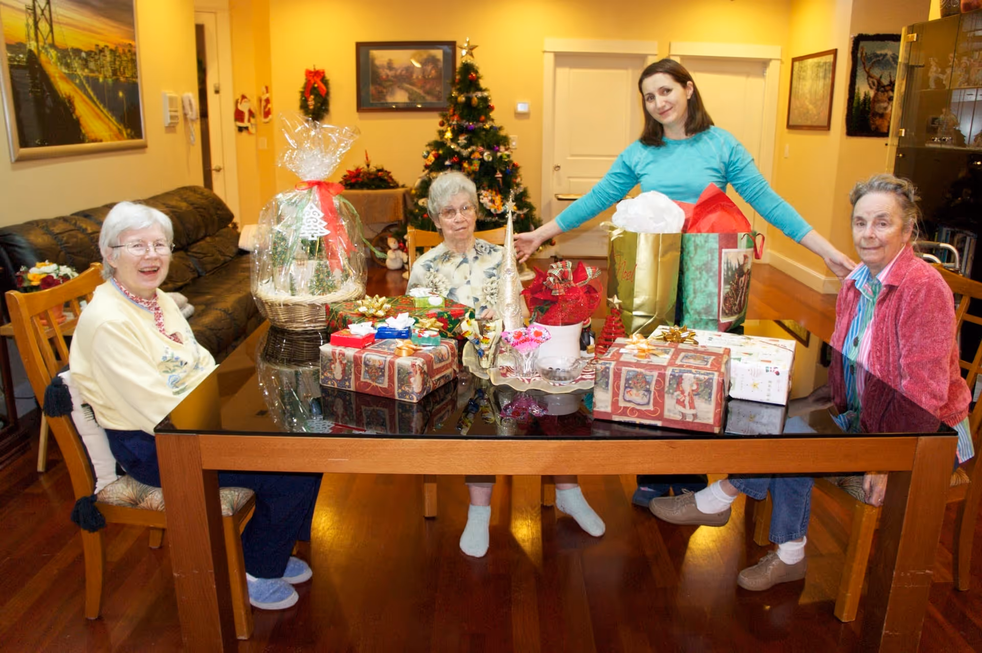 Four women sit around a table filled with wrapped Christmas gifts and decorations in a communal dining/living area.