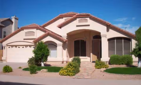 Front view of a tan, single-story retirement home with a curved entrance and landscaped yard.