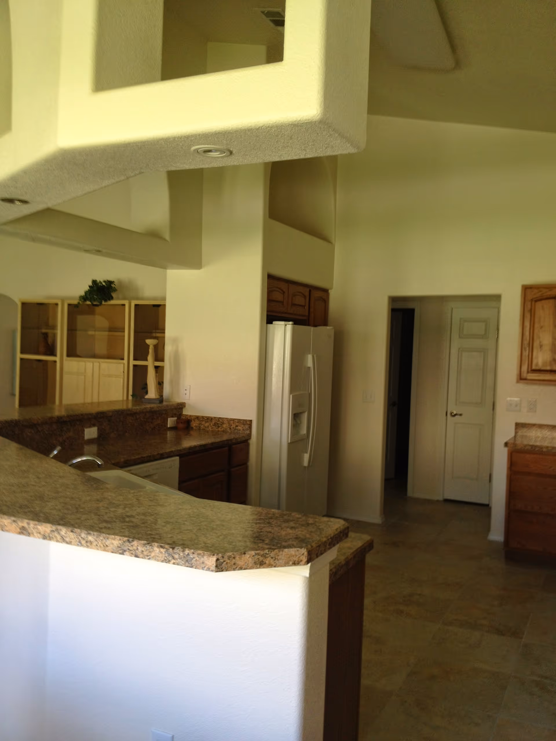 Open kitchen with granite countertops and raised breakfast bar, refrigerator, wooden cabinets, and tiled floor.