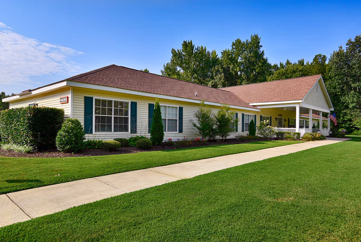 Single-story ranch-style building with a covered porch, green shutters, manicured lawn, and a sidewalk leading to the entrance.