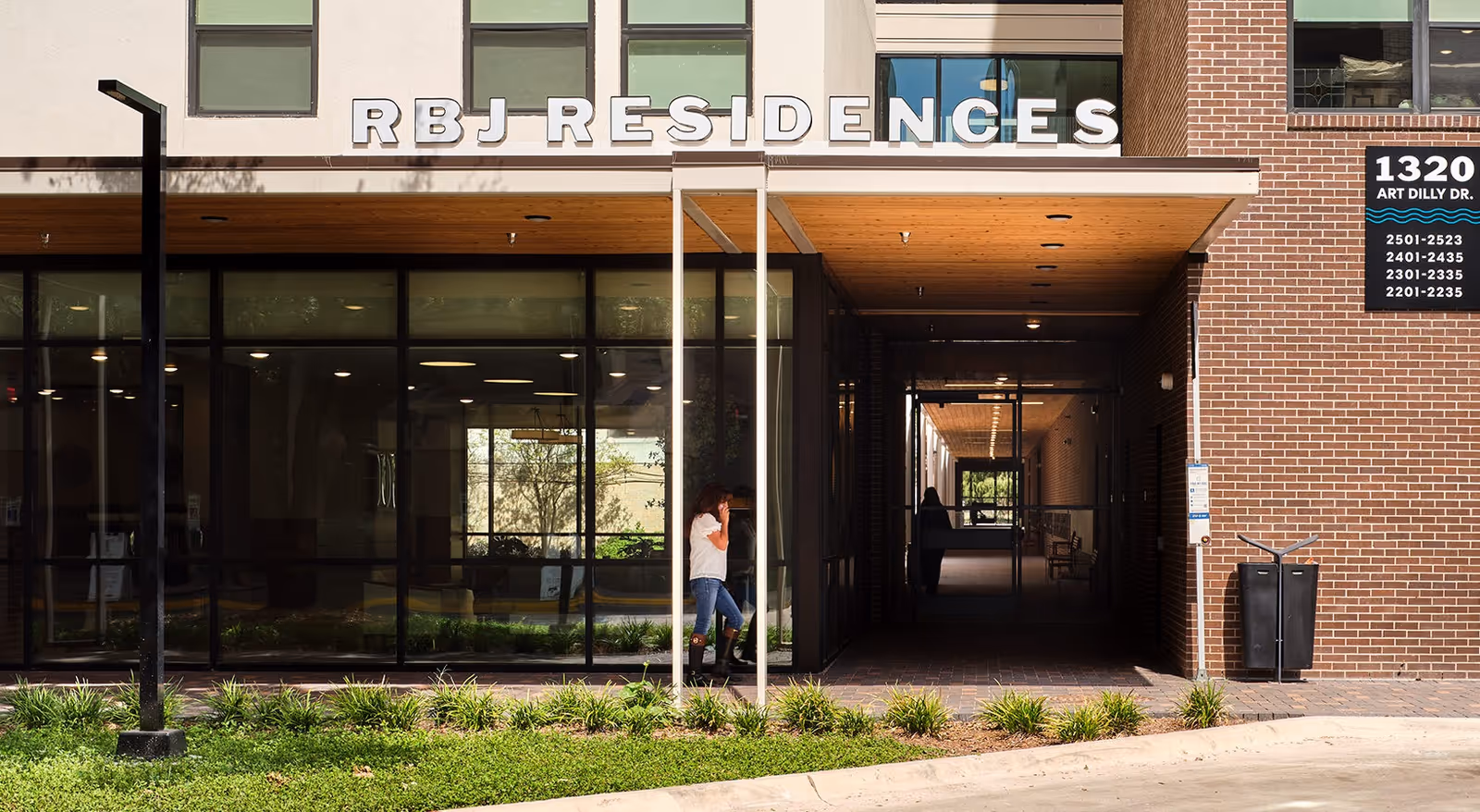 Exterior view of RBJ Residences senior housing with glass entry doors and two people at the entrance.