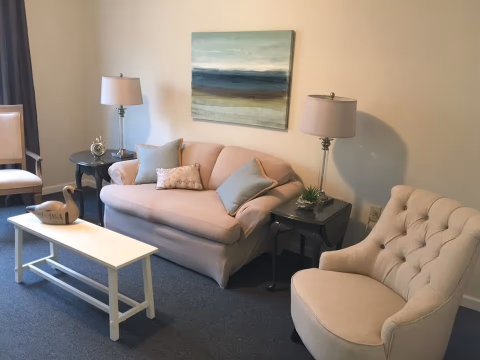 Cozy living room seating area with a blush loveseat, tufted armchair, side tables with lamps, a white coffee table and abstract wall art.