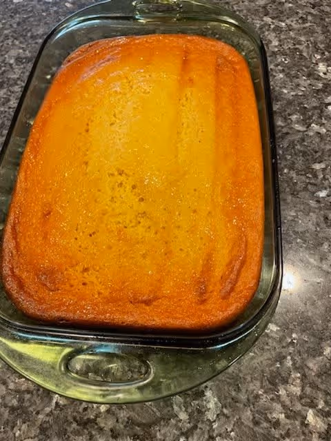 A freshly baked rectangular cake with a golden brown top in a clear glass baking dish placed on a granite countertop.