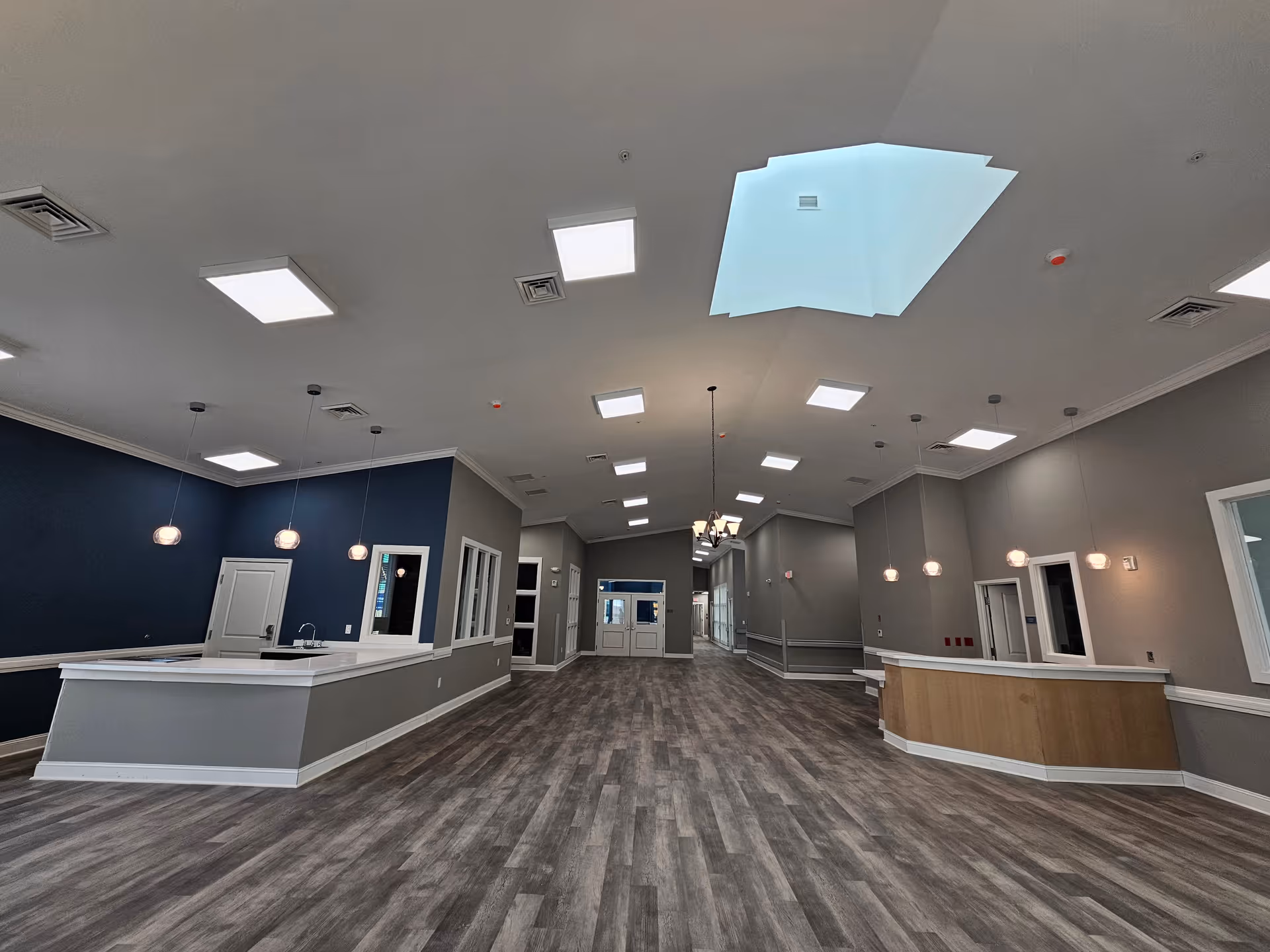 Spacious open interior lobby/reception area with high ceilings, pendant lights, a skylight, and wood-look flooring.