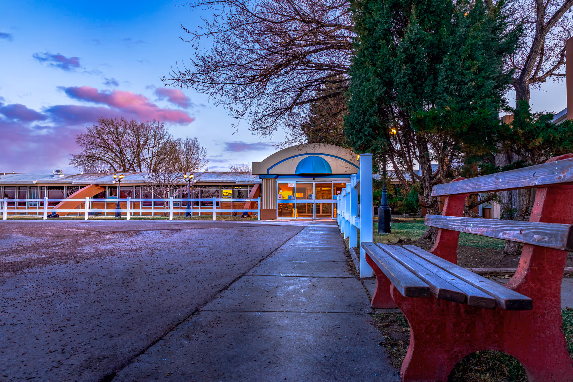 Exterior view of The Ivy at Great Falls entrance with a walkway, bench, and trees at dusk.