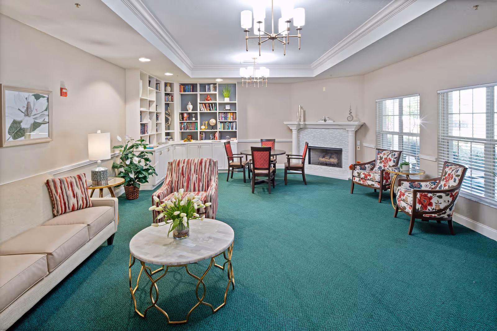 Bright communal living room with sofas, armchairs, a round coffee table, built-in bookshelves and a fireplace.