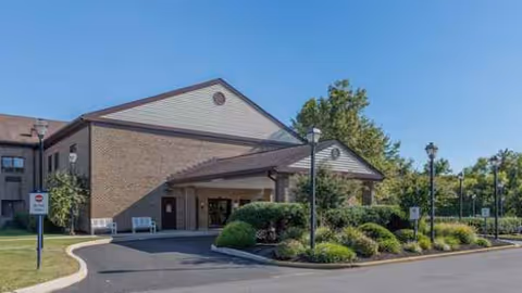 Exterior view of Atlas West Deptford senior living facility with entrance, shrubs, and parking.