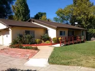 Front view of a single-story senior living facility with ramp and green lawn.