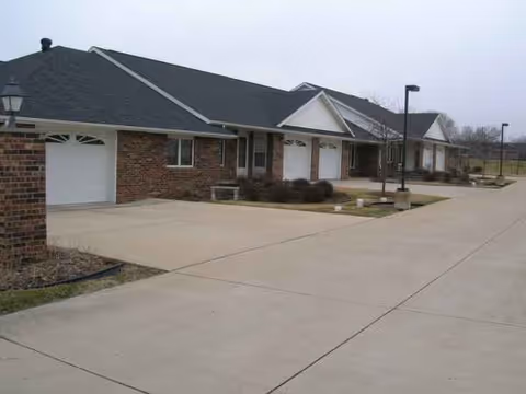 Single-story brick senior living facility with garages, a paved drive, and lampposts.