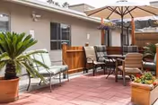 Outdoor patio with tables, chairs, umbrella, and potted plants beside a beige building.