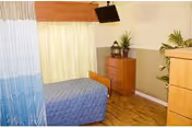 A senior living facility bedroom with a blue bed, curtains, dresser, and potted plants.