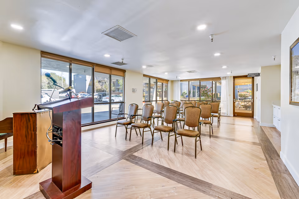 Bright meeting room with rows of chairs facing a wooden podium in front of large windows.