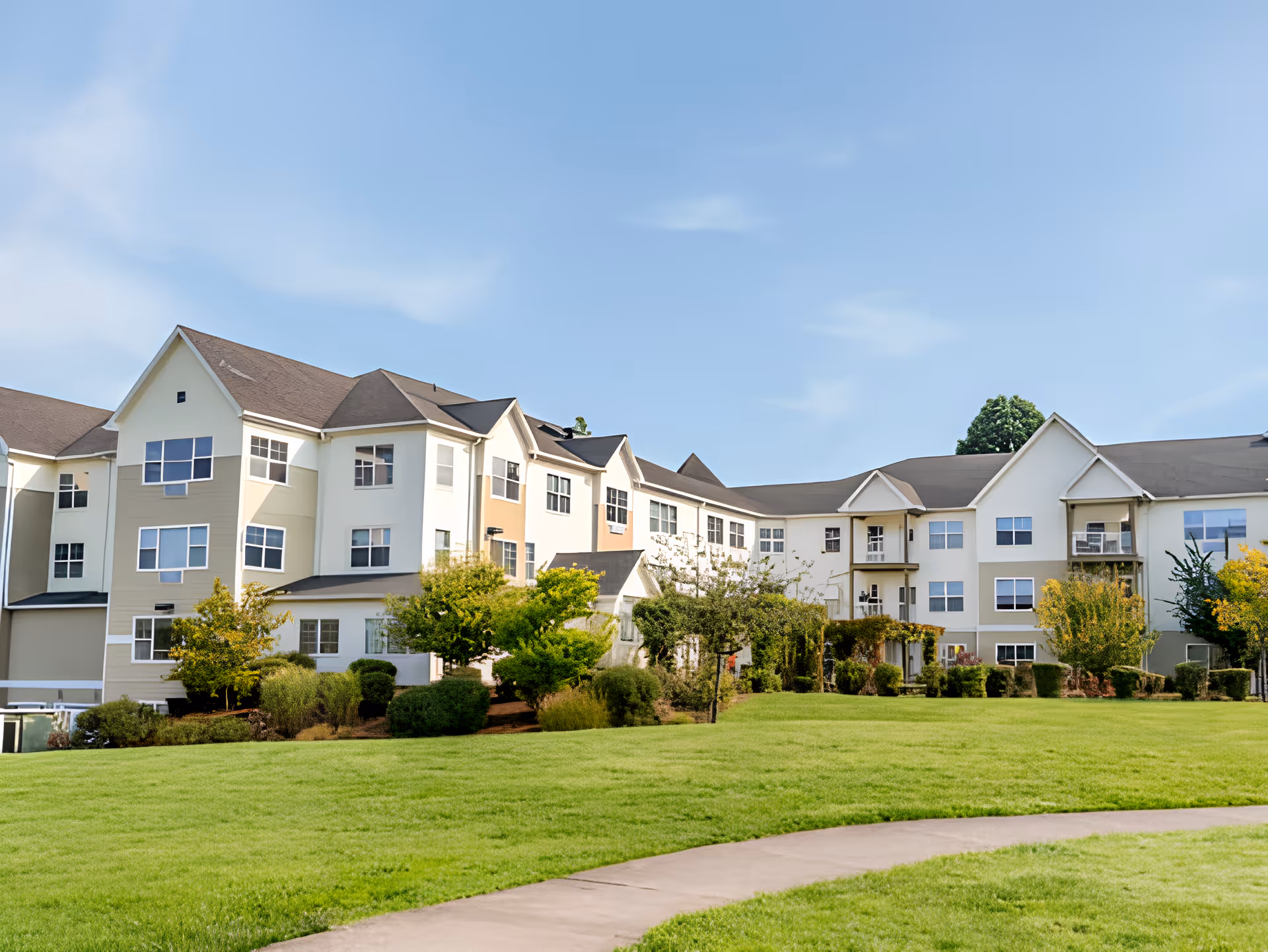 Front exterior of a multi-story senior living building with landscaped lawn and a curved walkway.
