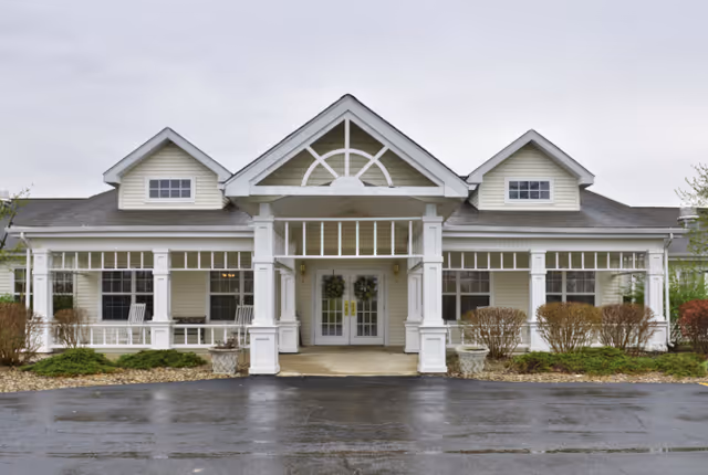 Exterior front entrance of a single-story building with a covered porch, white columns, double glass doors, and decorative windows.