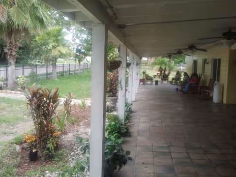 Covered outdoor patio at Lake Alfred Assisted Living with seating, ceiling fans, and planters.