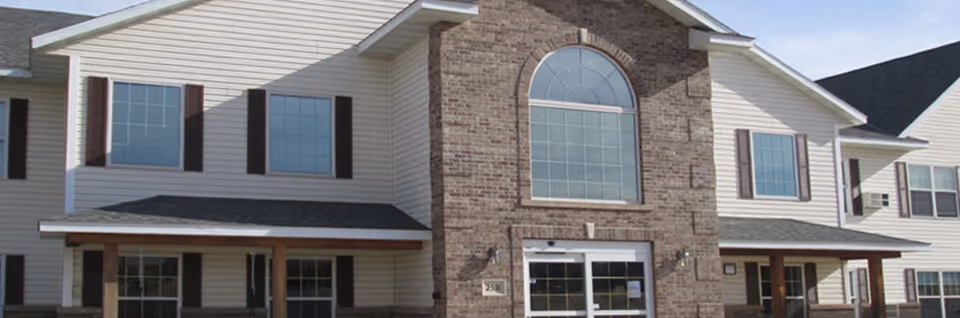 Front exterior of a two-story senior living building with a brick central entrance and white siding.