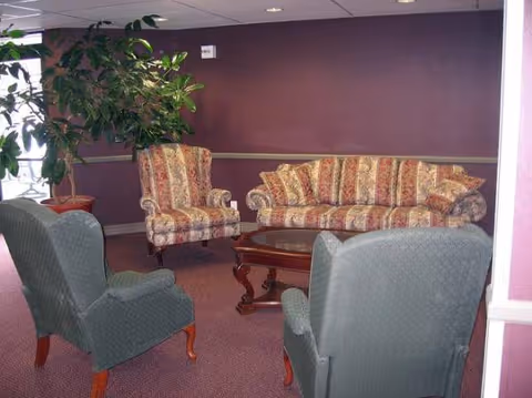 Purple-walled lounge with patterned sofas, chairs, a coffee table, and a potted plant.