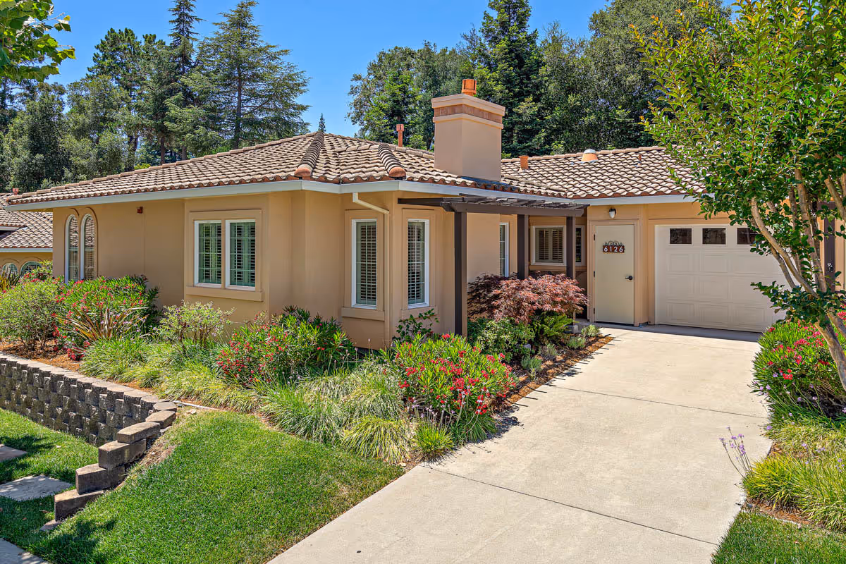 Single-story beige house with a tiled roof, attached garage and landscaped front yard beside a concrete driveway.