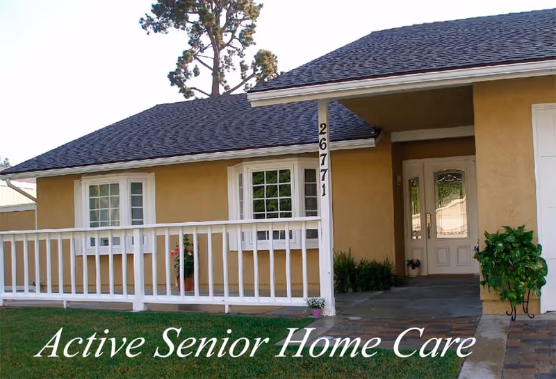 Front exterior view of a single-story house with beige walls, a dark shingled roof, white framed windows, a white railing along the porch, and a white front door. The house number 26771 is displayed on a white post near the entrance. There are some potted plants near the door and on the porch. The text 'Active Senior Home Care' is overlaid at the bottom of the image.