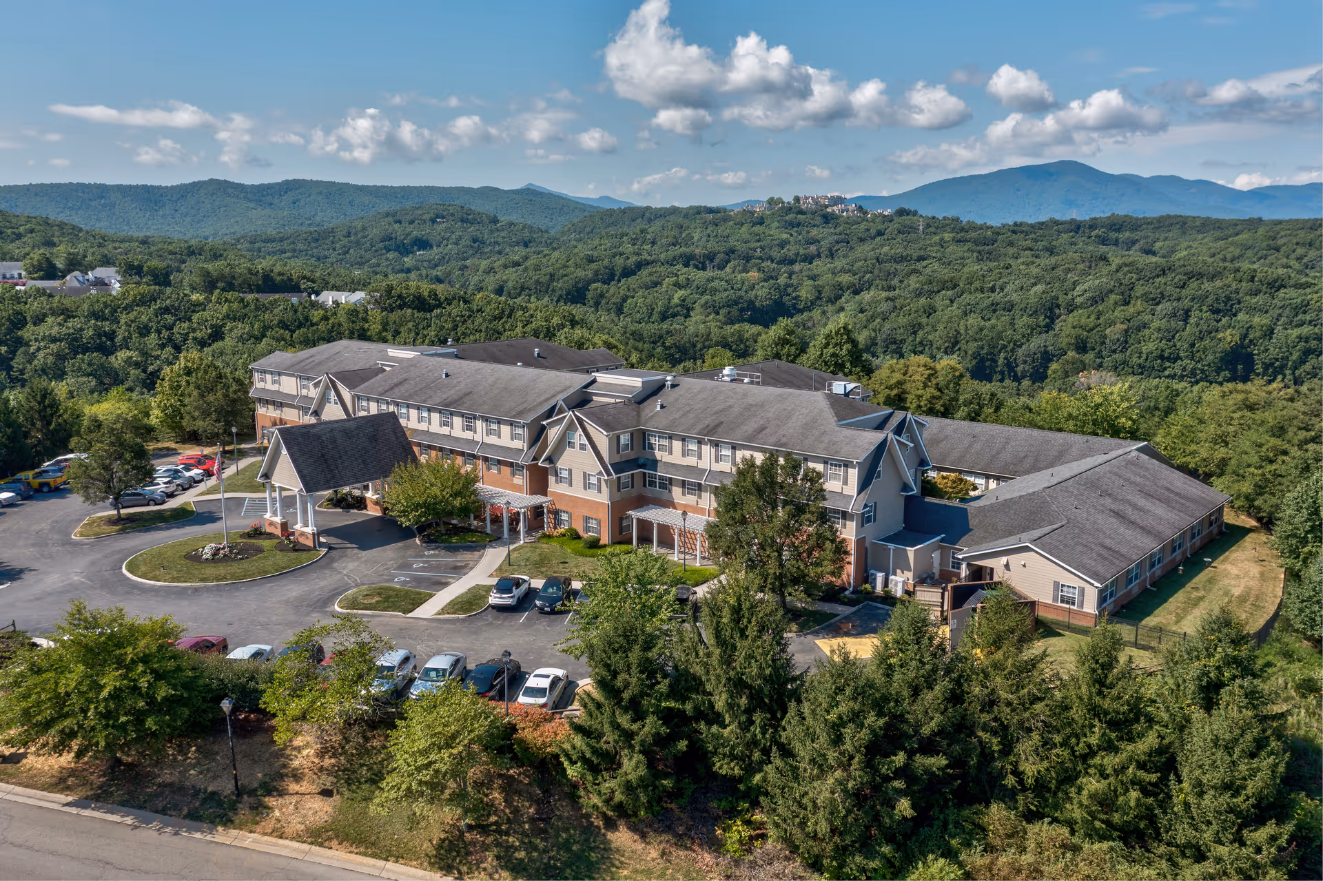 Aerial view of the TerraBella Pheasant Ridge senior living building surrounded by trees and distant mountains.