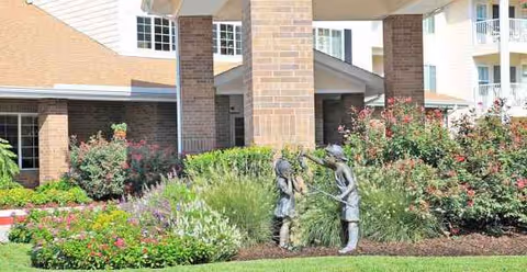 Exterior view of Cypress Woods Sky Active Living with brick columns, entrance, and landscaped garden statues.