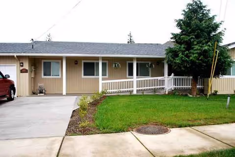Single-story beige senior living home with front porch, green lawn, driveway.