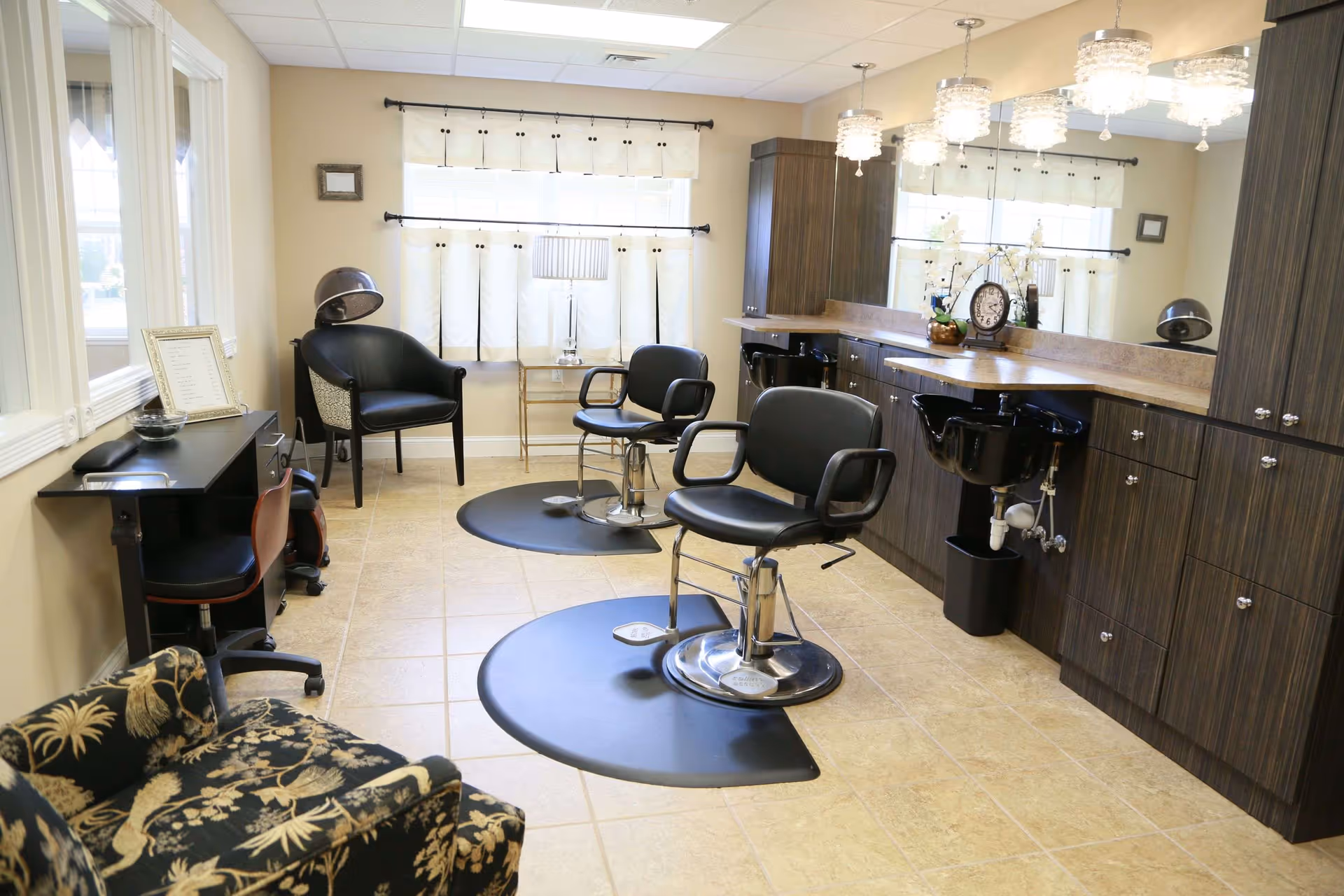 A bright salon-style room with two styling chairs, shampoo sinks, mirrors, and cabinetry.