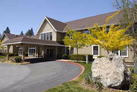 Exterior view of Hilltop Commons Senior Living building with trees and a large rock.