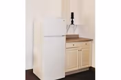 A small white refrigerator next to a beige cabinet with a wooden countertop, topped with a black candlestick holder, against a plain white wall.
