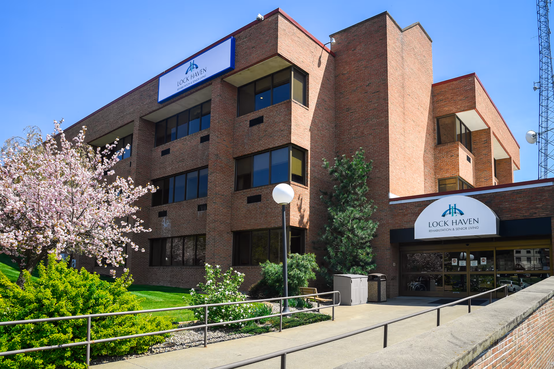Brick exterior and front entrance of Lock Haven Rehabilitation & Senior Living with landscaping and a flowering tree.