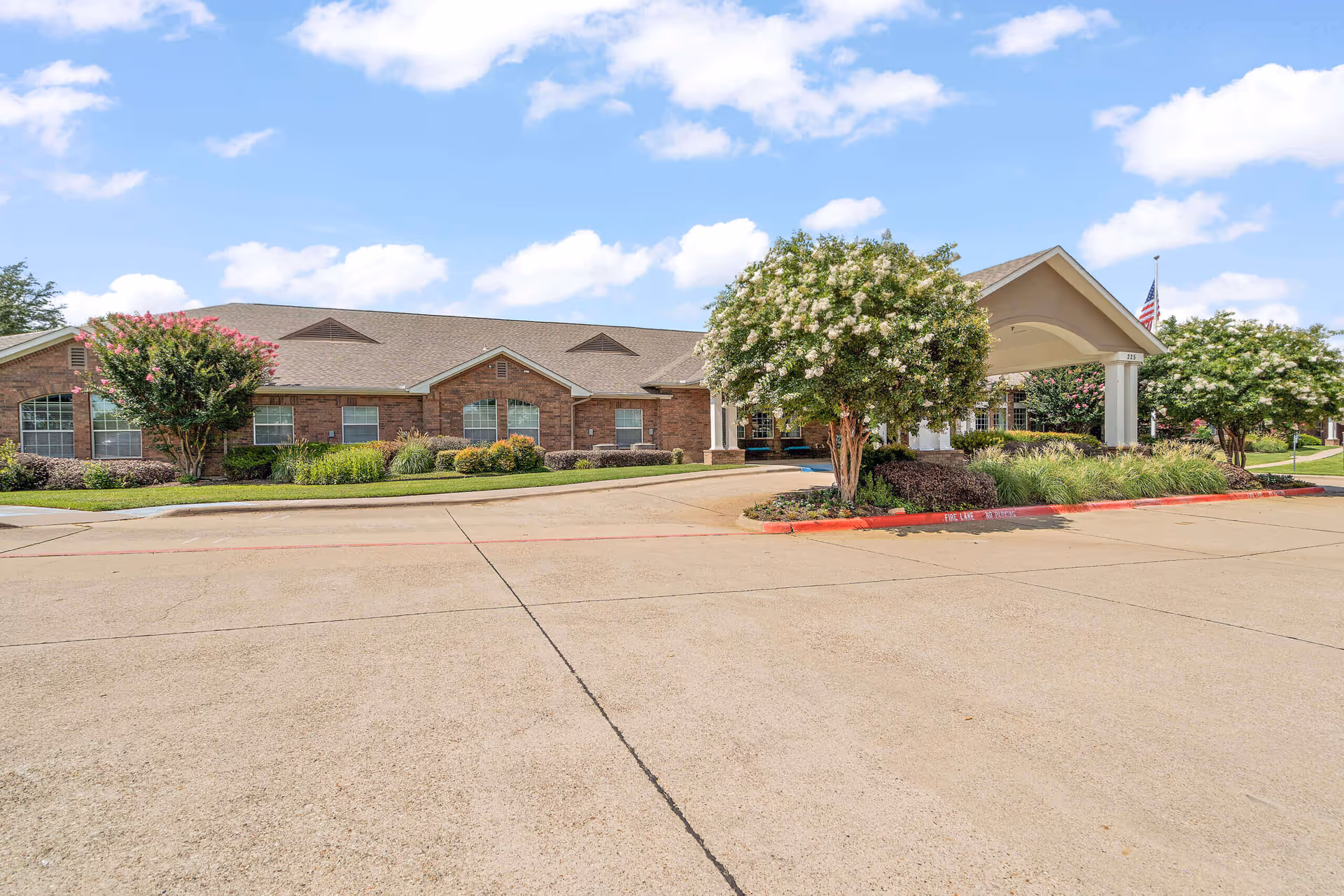 Exterior view of Morada Cedar Hill featuring a brick facade, landscaped entrance, and flowering trees.