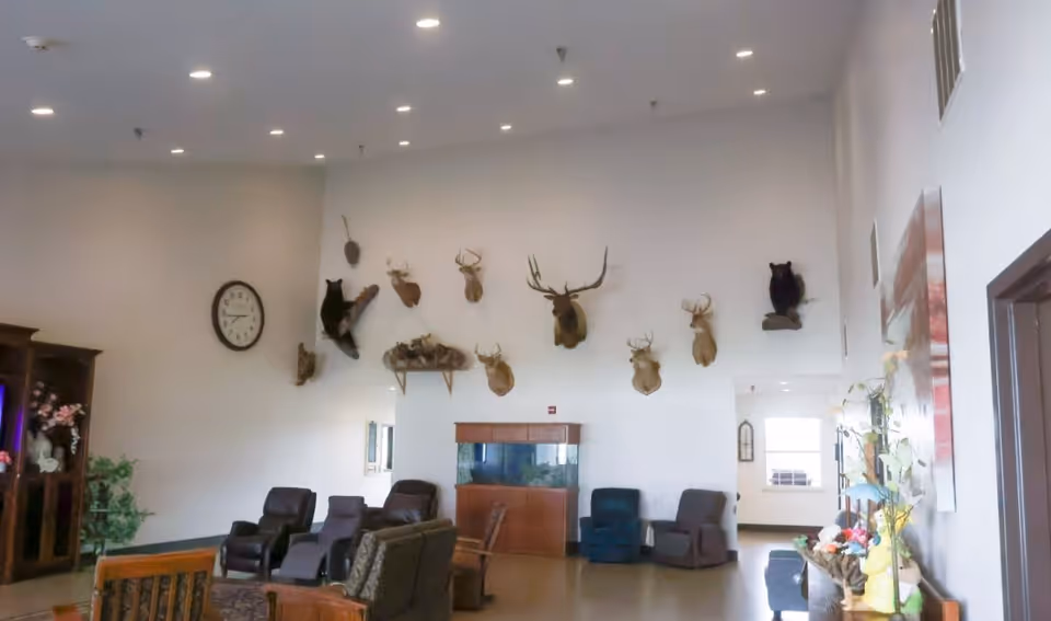 Interior senior living lounge with scattered chairs, a wall clock, fish tank, and mounted deer heads.