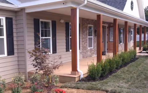 Exterior view of a single-story senior living facility with a covered walkway and shrubs.