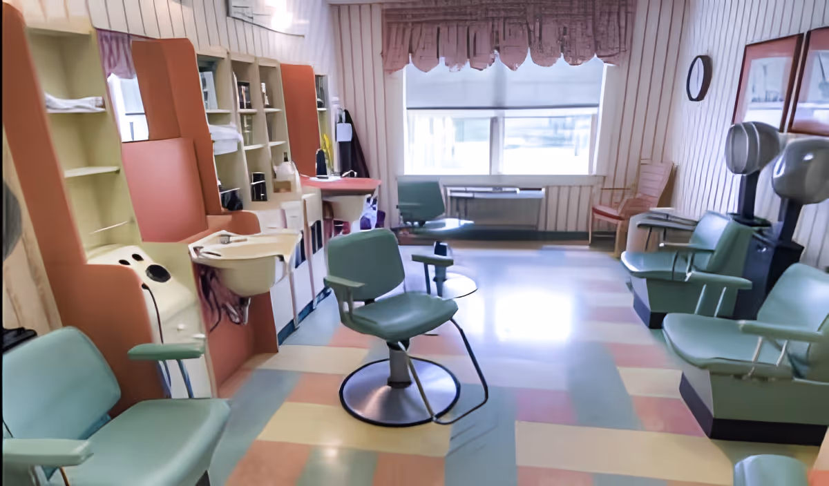 Salon-style room with mint-green styling chairs, hair-washing sinks, and hooded dryers in a pastel-tiled interior.