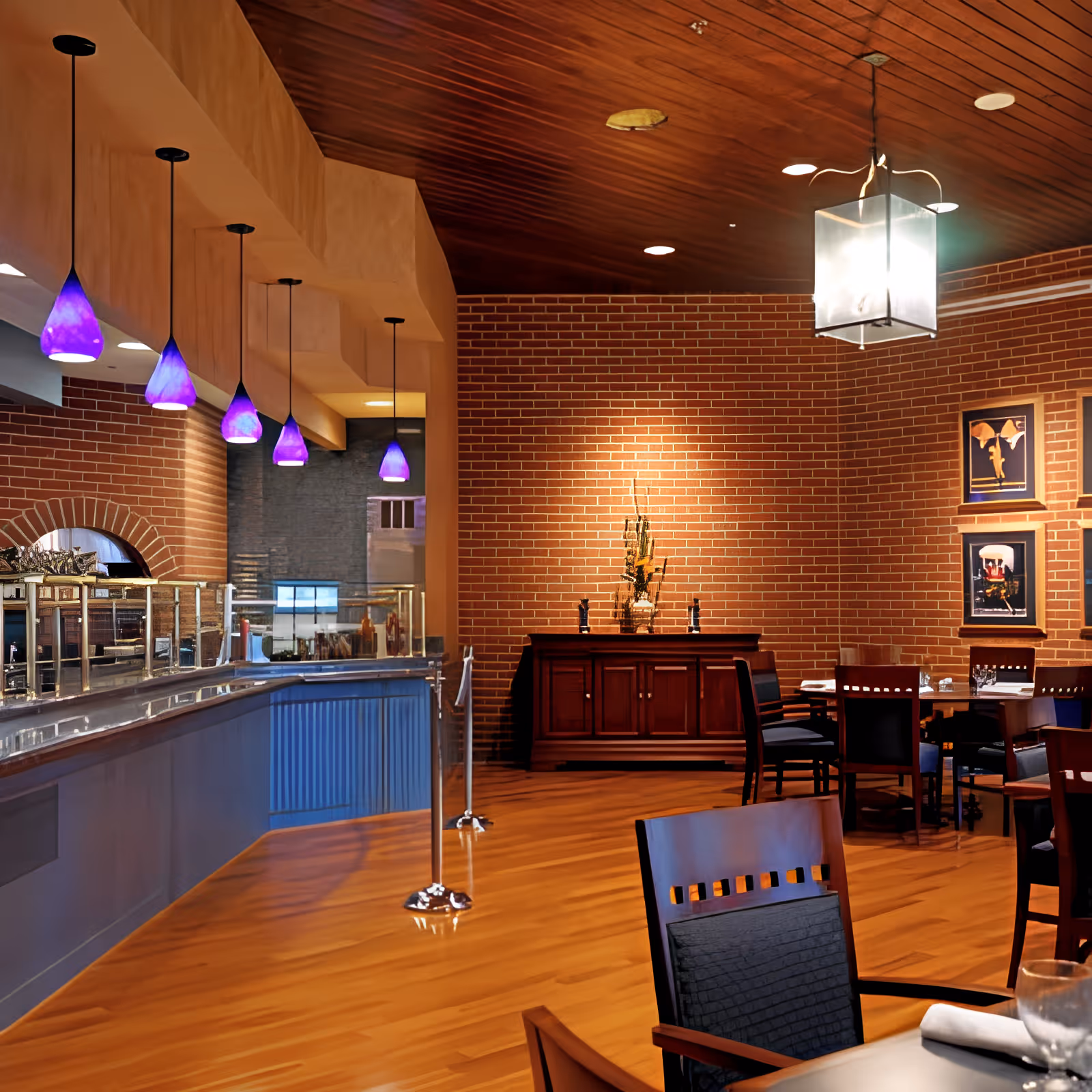 Interior dining room with wooden floors and brick walls, purple pendant lights, a buffet counter, and dining tables and chairs.
