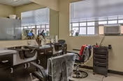 Interior salon area with two barber chairs, a large mirror, styling stations and a window with blinds.