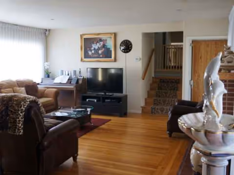Golden Age Retirement Home living room with leather seating, TV, piano, and staircase.