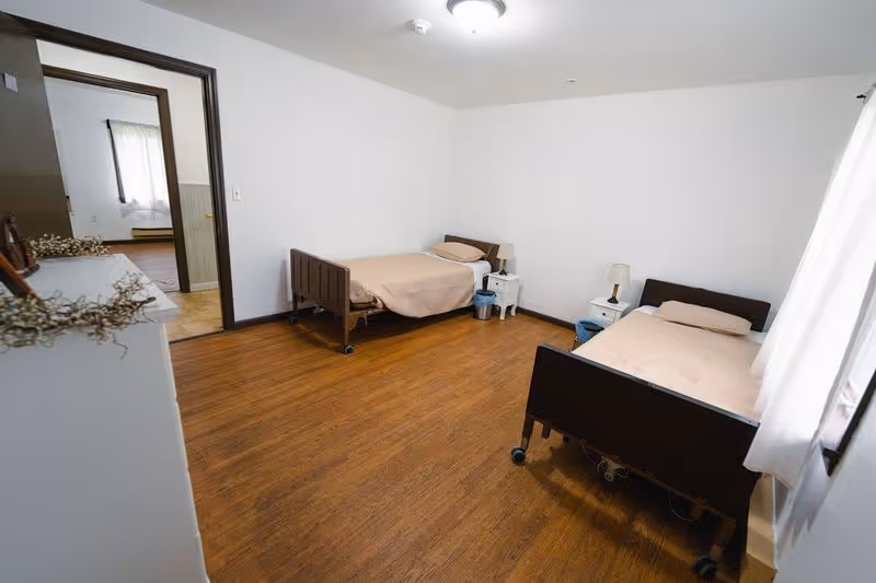 Sparsely furnished bedroom with two single beds, bedside tables, hardwood floors and white walls.