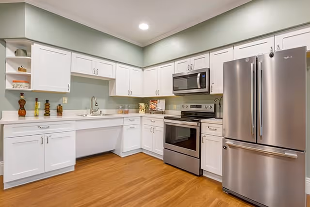 Modern kitchen with white cabinets, stainless steel appliances, and wood-look flooring.